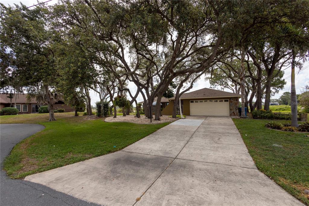 A concrete driveway leads to the garage of a house shaded by large oak trees — 268 EASTPOINT COURT, SPRING HILL, FL