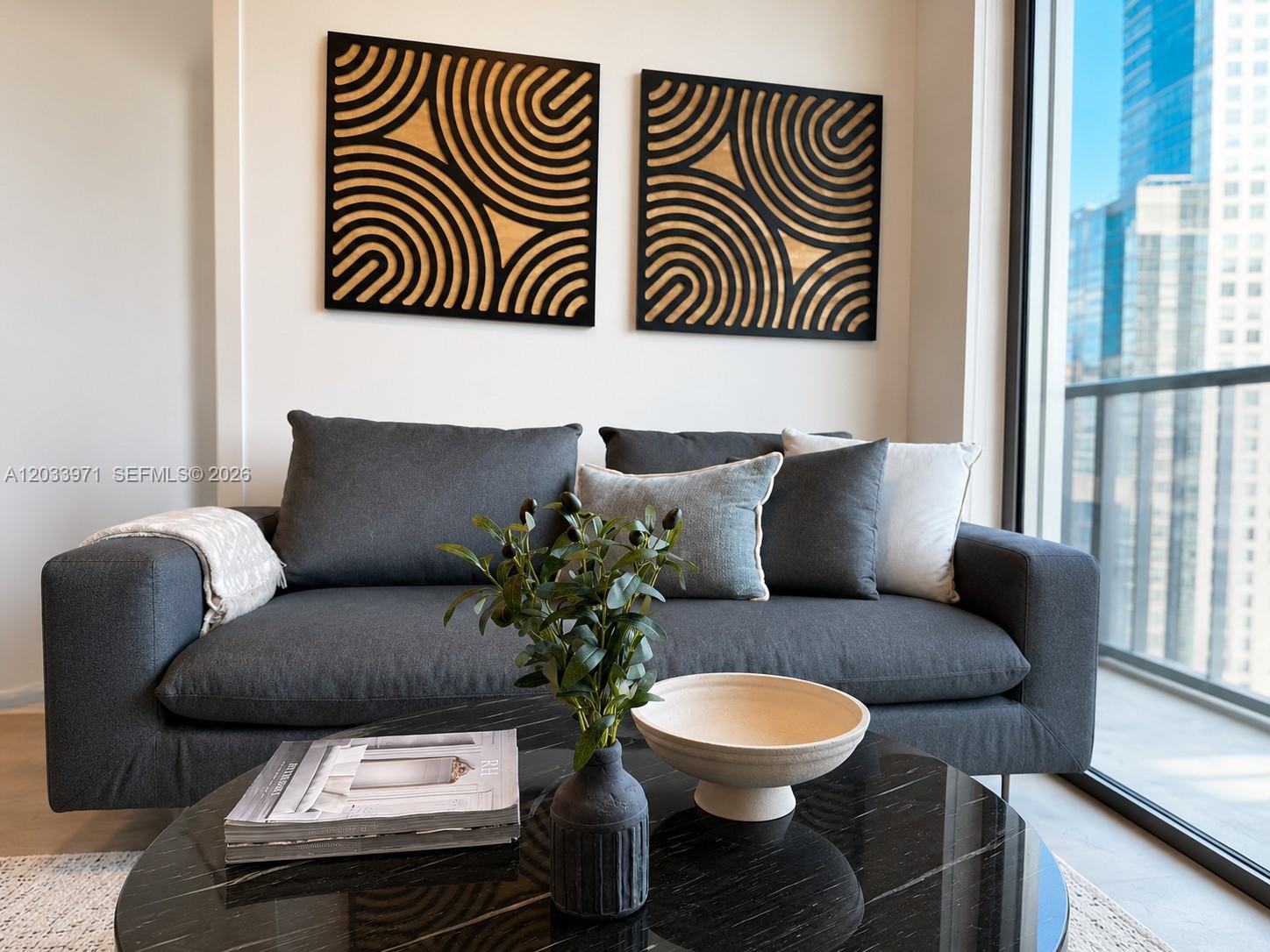 A modern living room features a dark gray sofa, circular coffee table, and geometric wall art — 121 NE 5th St # 3002, Miami FL 33132, MIAMI, FL