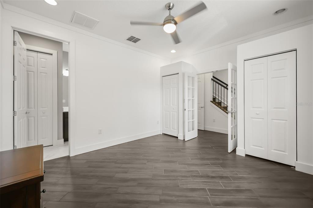 A bedroom with white walls, dark wood-look tile flooring, a ceiling fan, and multiple doors — 789 GREYBULL RUN, LAKE MARY, FL