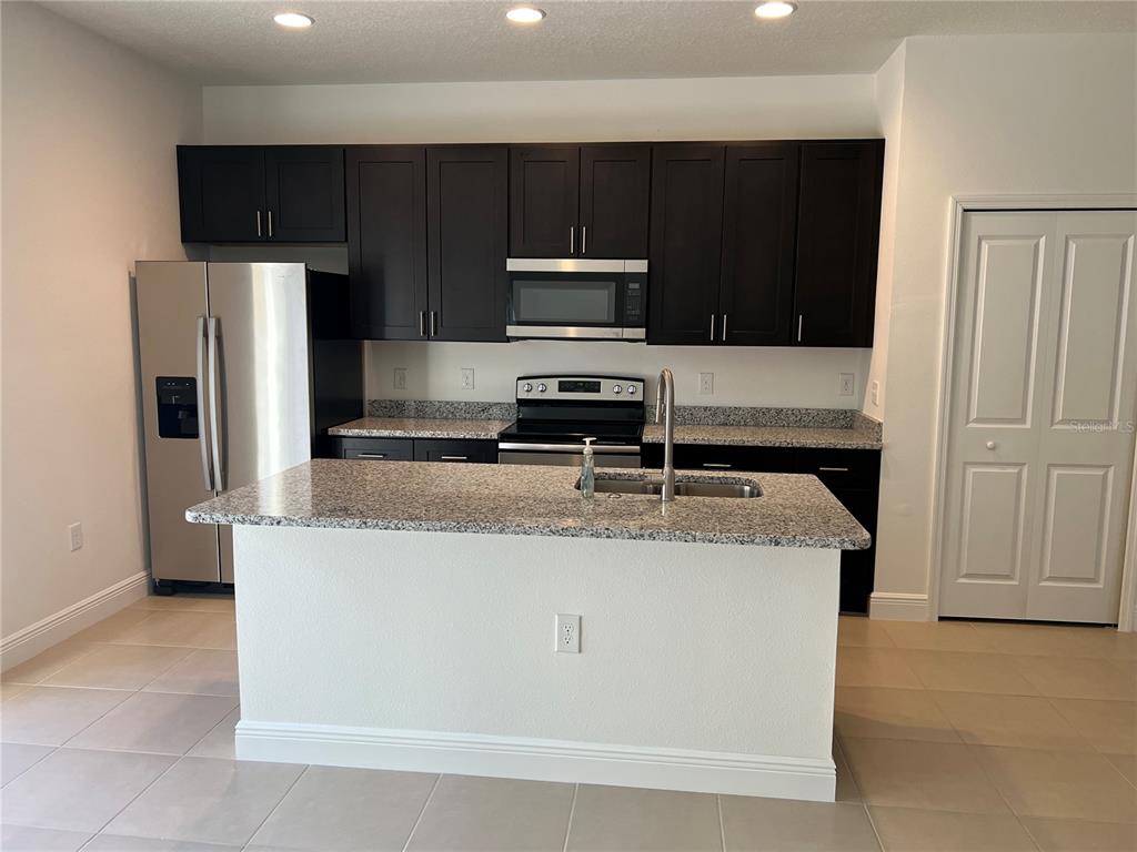 A kitchen features dark wood cabinets, granite countertops, stainless steel appliances, and a central island — 7260 SW 132ND PLACE, OCALA, FL