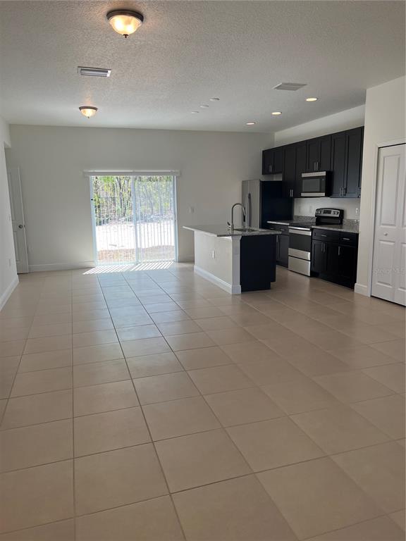 An open-concept kitchen with dark cabinets and an island overlooks a tiled living area — 7260 SW 132ND PLACE, OCALA, FL