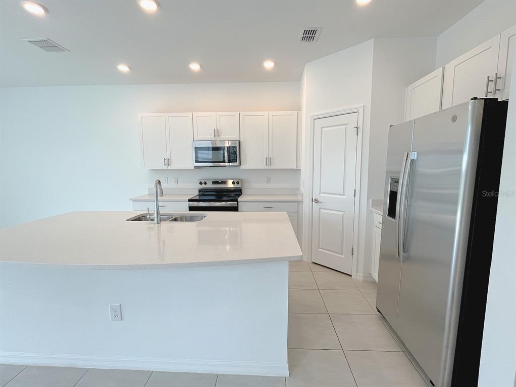 A modern kitchen features white cabinets, stainless steel appliances, and a large quartz-topped island — 11832 GLENSIDE TERRACE, PALMETTO, FL
