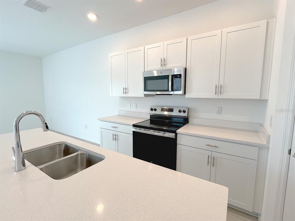 A modern kitchen features white cabinets, stainless steel appliances, and a large quartz-topped island — 11832 GLENSIDE TERRACE, PALMETTO, FL