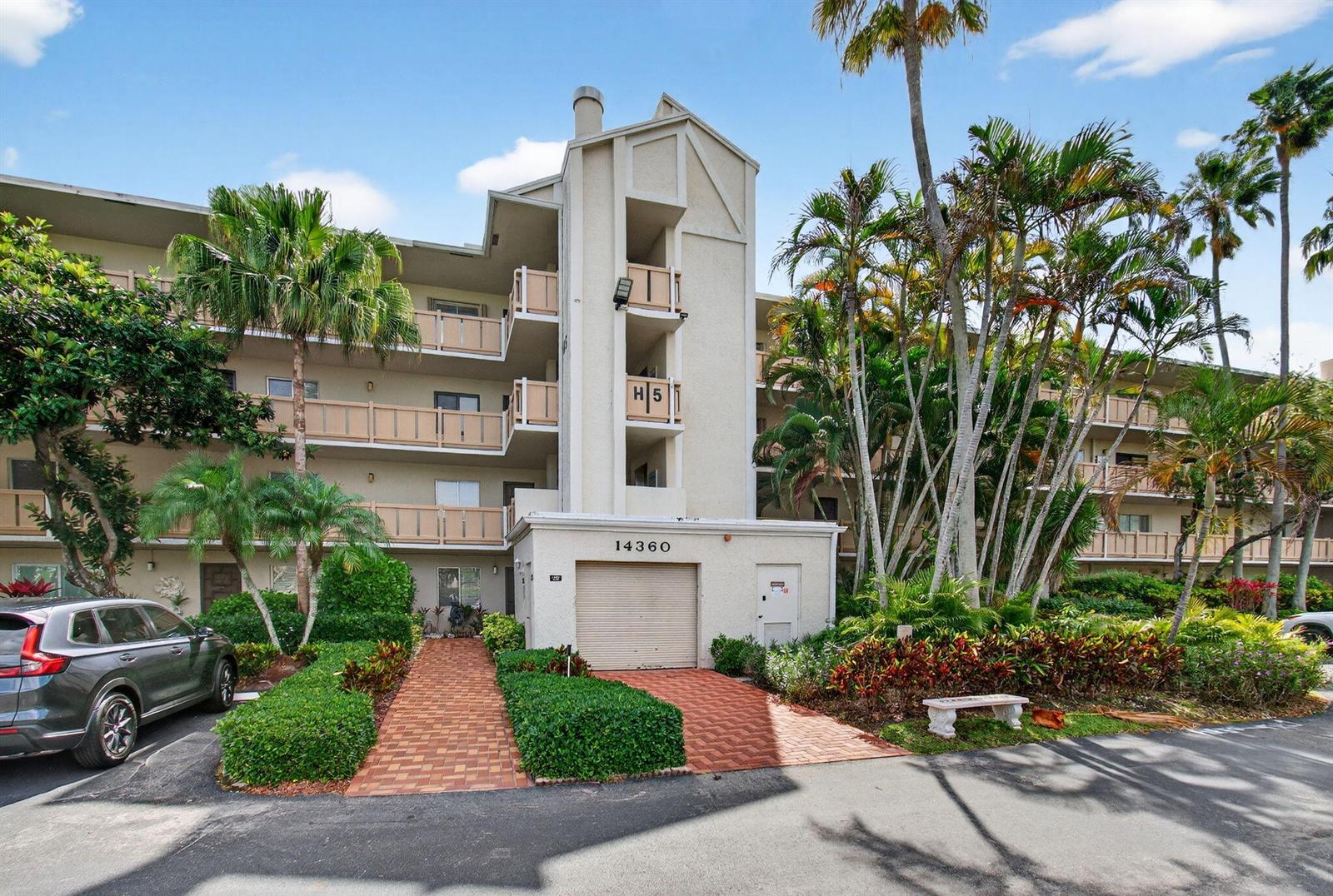 A multi-story apartment building features a beige facade, balconies, and a ground-level garage — 14360 Strathmore Lane # 406, Delray Beach FL 33446, DELRAY BEACH, FL