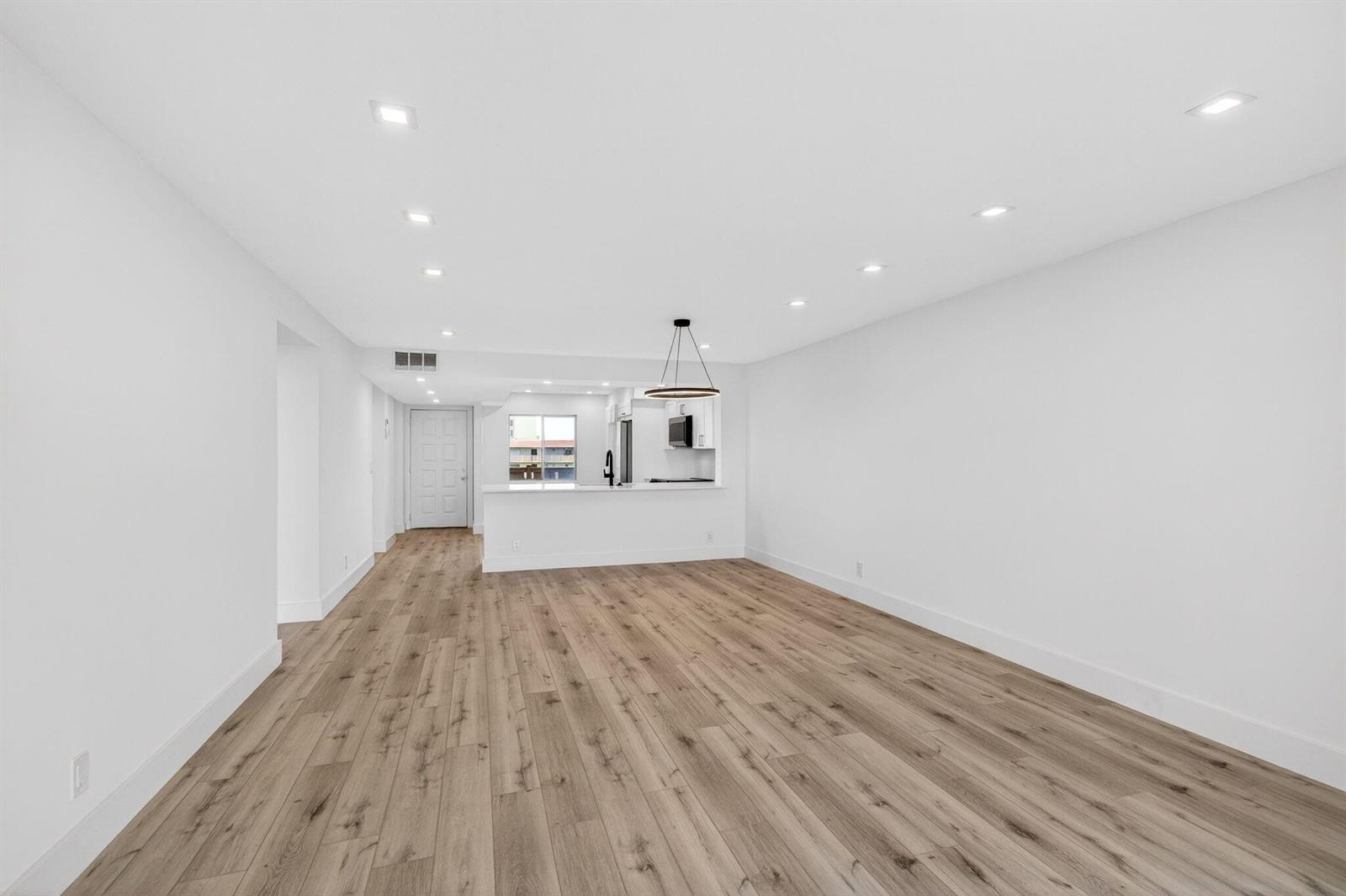 A bright, open-concept living area features light wood-look flooring, recessed lighting, and a kitchen pass-through — 14360 Strathmore Lane # 406, Delray Beach FL 33446, DELRAY BEACH, FL