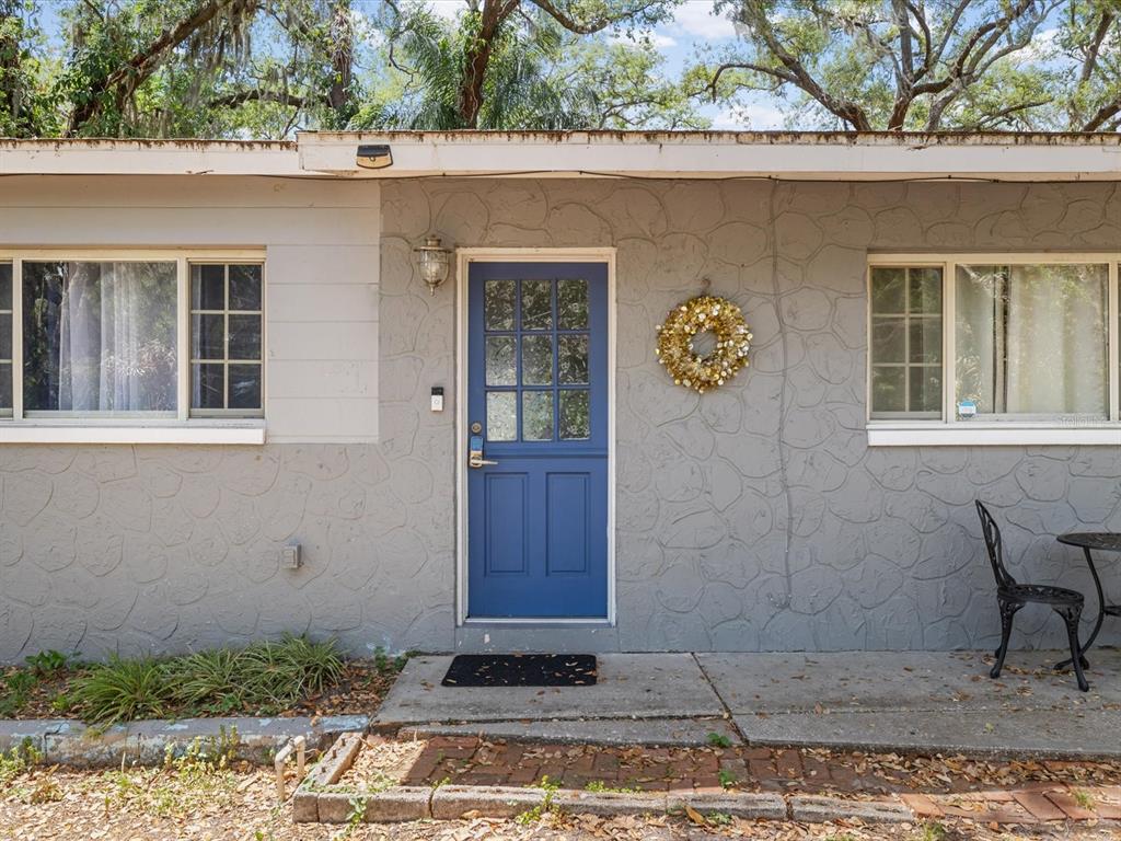 A gray house exterior features a blue front door, two windows, and a small patio — 8512 N 29TH STREET, TAMPA, FL