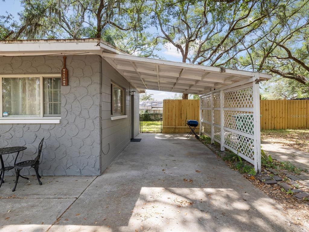 A gray house exterior features a concrete patio covered by a white wooden carport — 8512 N 29TH STREET, TAMPA, FL