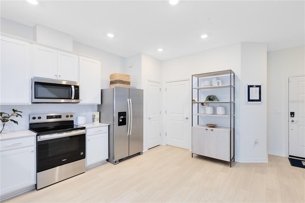A kitchen with white cabinets, stainless steel appliances, light wood flooring, and a metal shelving unit — 4405 JETTY LANE NE, PALM BAY, FL