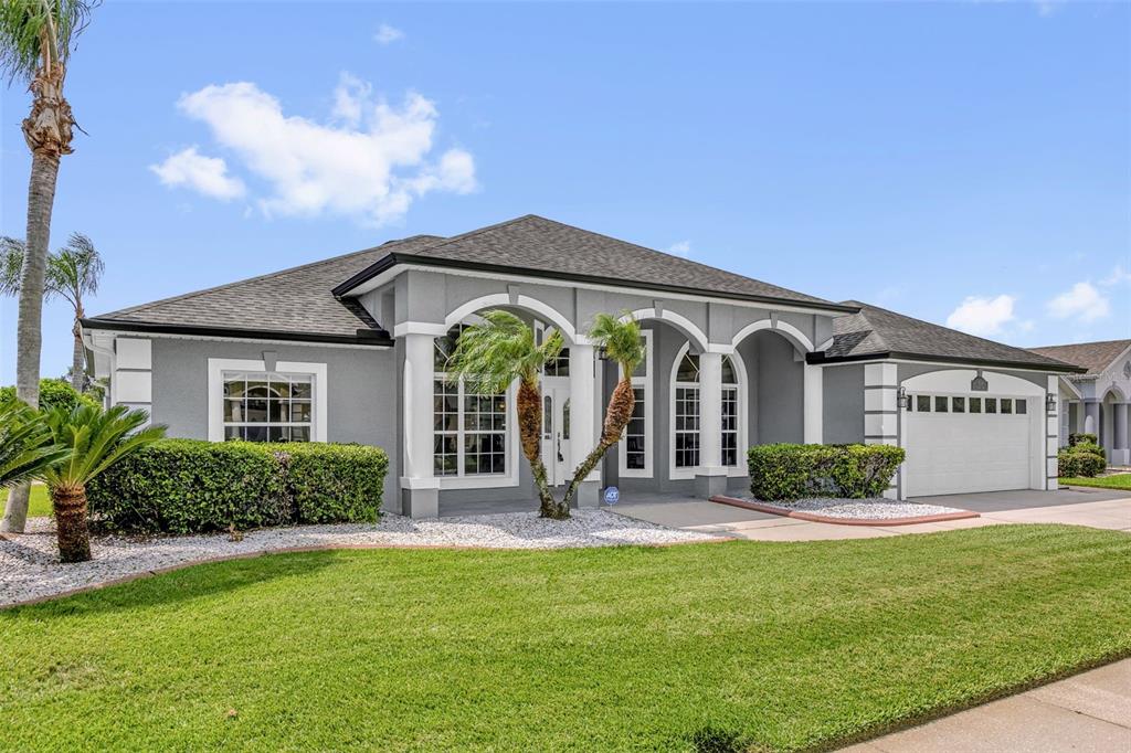 A gray single-story house with a white garage, arched windows, and a manicured front lawn — 1934 FAIRWAY LOOP, KISSIMMEE, FL