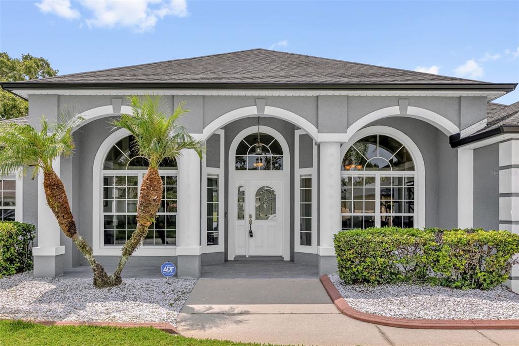 The exterior of a gray house features a white arched entryway, large windows, and palm trees — 1934 FAIRWAY LOOP, KISSIMMEE, FL
