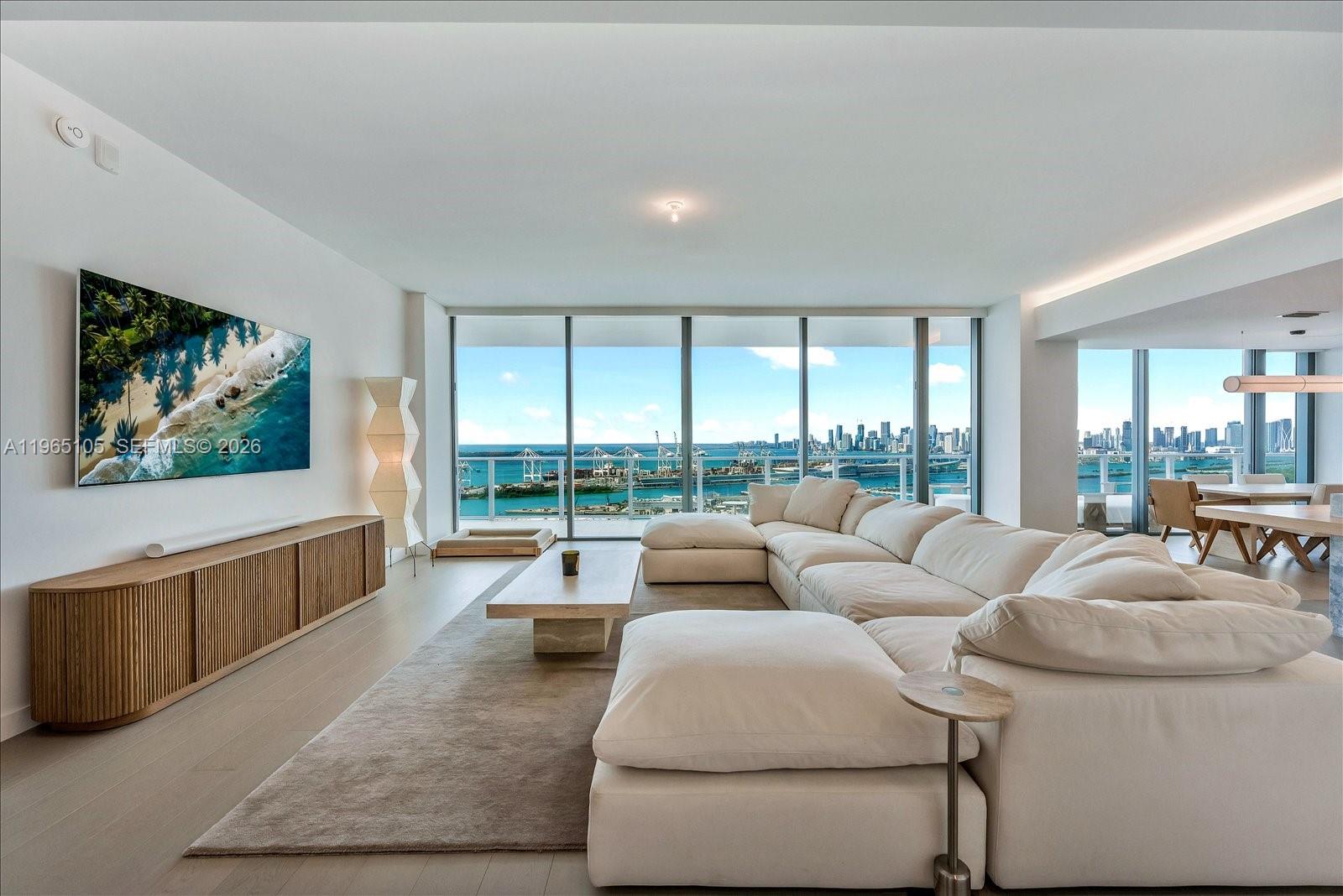 A modern living room features a large white sectional, wood media console, and floor-to-ceiling windows — 501 West Ave # 3102, Miami Beach FL 33139, MIAMI BEACH, FL