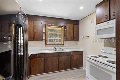 A kitchen features dark wood cabinets, white countertops, and white appliances — 420 N FAIRVIEW AVENUE, DELAND, FL