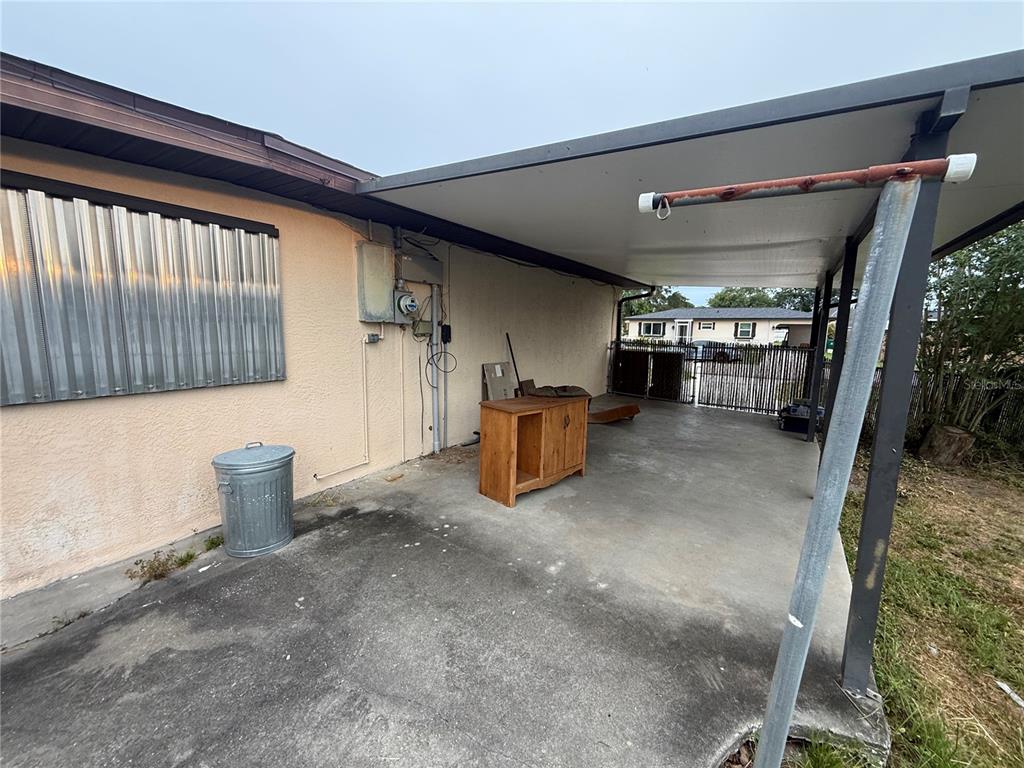 A concrete carport features a metal roof, a wooden cabinet, and a metal trash can — 23014 MCNULTY AVENUE, PORT CHARLOTTE, FL