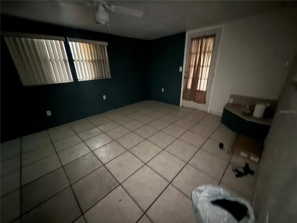 An empty room features dark walls, light-colored floor tiles, a ceiling fan, and a glass door — 23014 MCNULTY AVENUE, PORT CHARLOTTE, FL