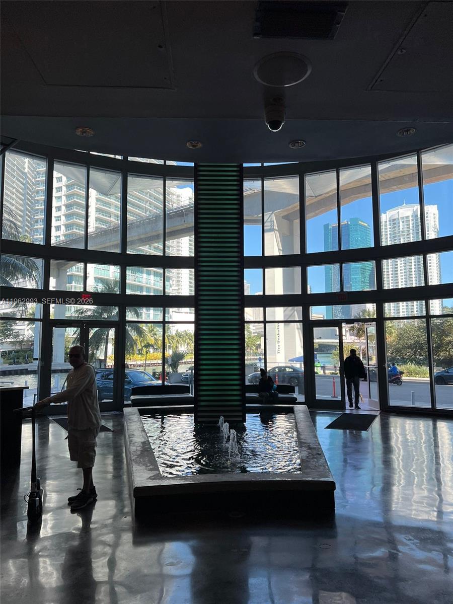 A lobby features a central water fountain, floor-to-ceiling windows, and views of urban buildings — 690 SW 1st Ct # 1506, Miami FL 33130, MIAMI, FL