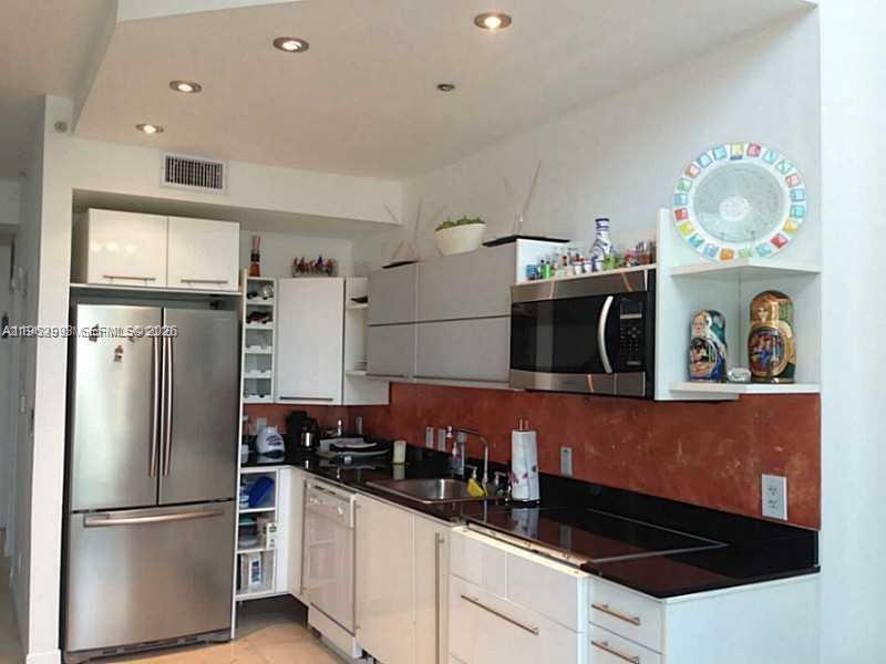 A modern kitchen features stainless steel appliances, white cabinetry, black countertops, and a copper-toned backsplash — 690 SW 1st Ct # 1506, Miami FL 33130, MIAMI, FL