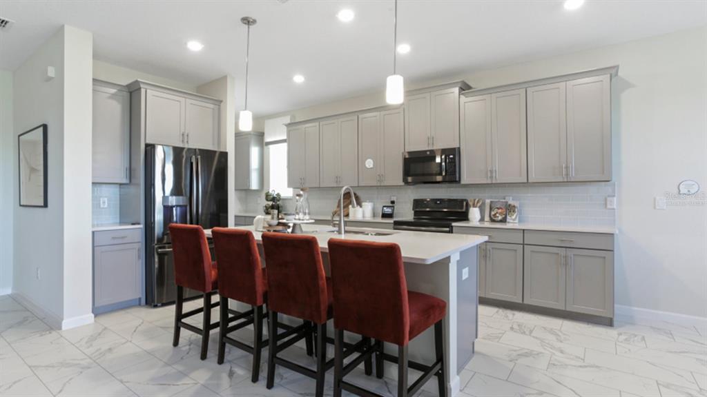 A kitchen features gray cabinets, white countertops, a central island with red stools, and tile flooring — 3116 NAMASTE DRIVE, CLERMONT, FL