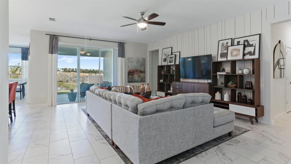 A living room features a gray sectional sofa, a television, shelving, and sliding glass doors — 3116 NAMASTE DRIVE, CLERMONT, FL