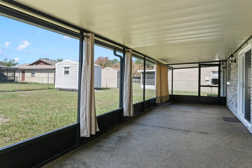 A screened-in porch with a concrete floor, beige curtains, and a view of the backyard — 11403 FILLMORE AVENUE, SEFFNER, FL