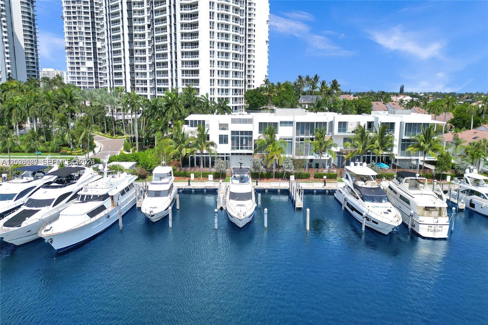 An aerial view shows several yachts docked in a marina in front of modern buildings — AVENTURA, FL