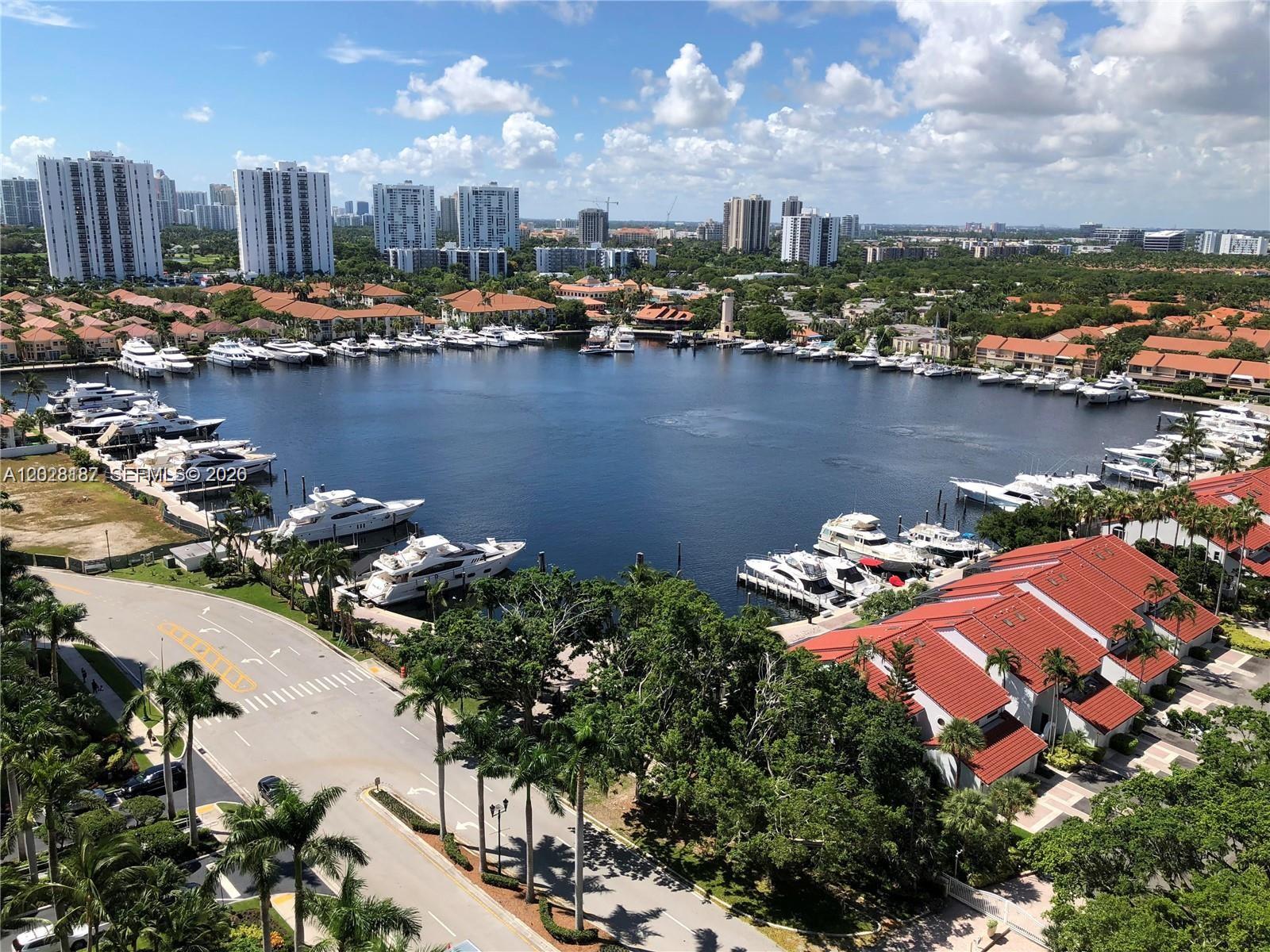 An aerial view shows a marina filled with yachts surrounded by residential buildings and trees — AVENTURA, FL