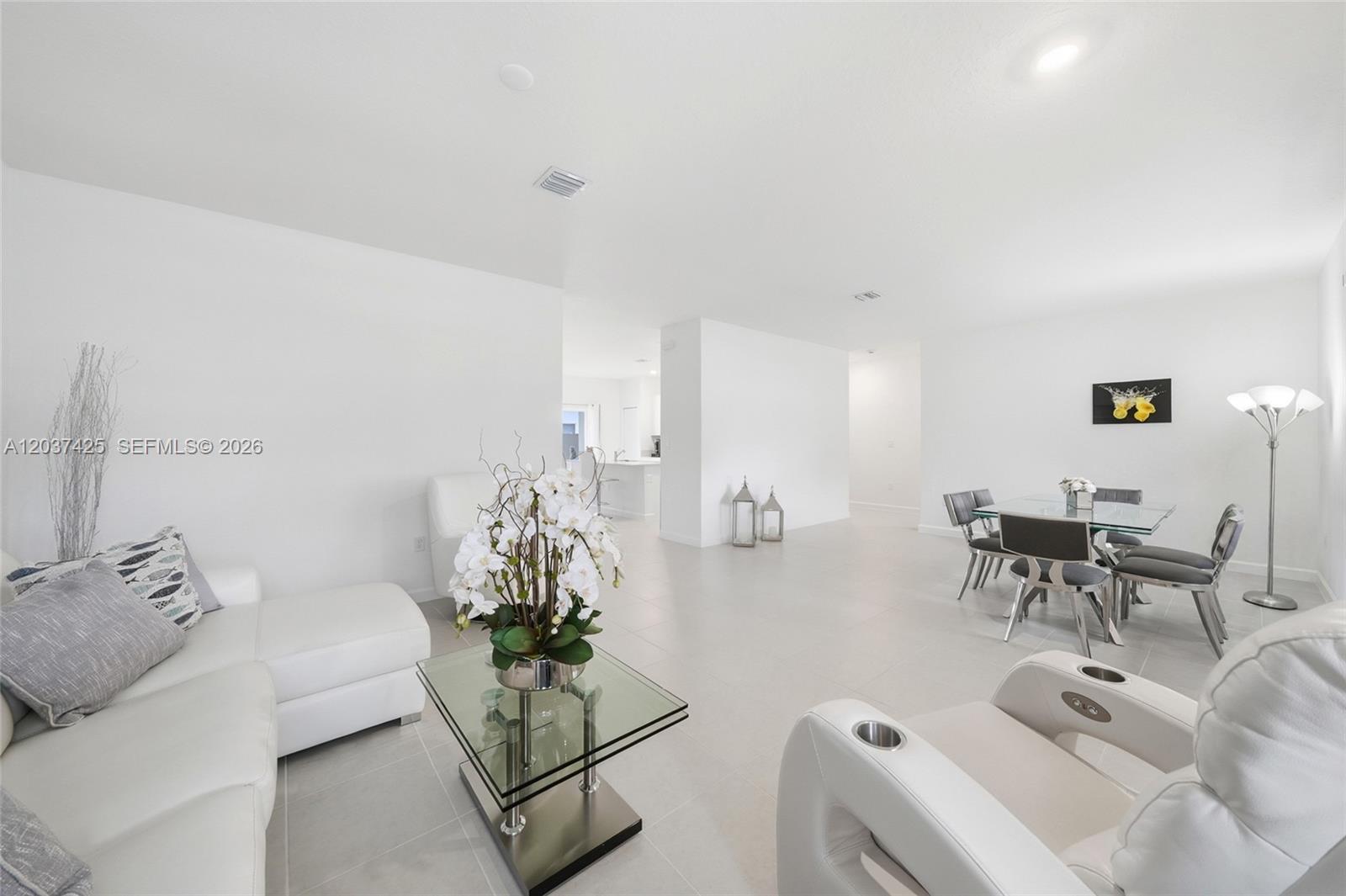 A bright, open-concept living and dining area features white furniture, tile floors, and modern decor — 13249 SW 189th Ter, Miami FL 33177, MIAMI, FL