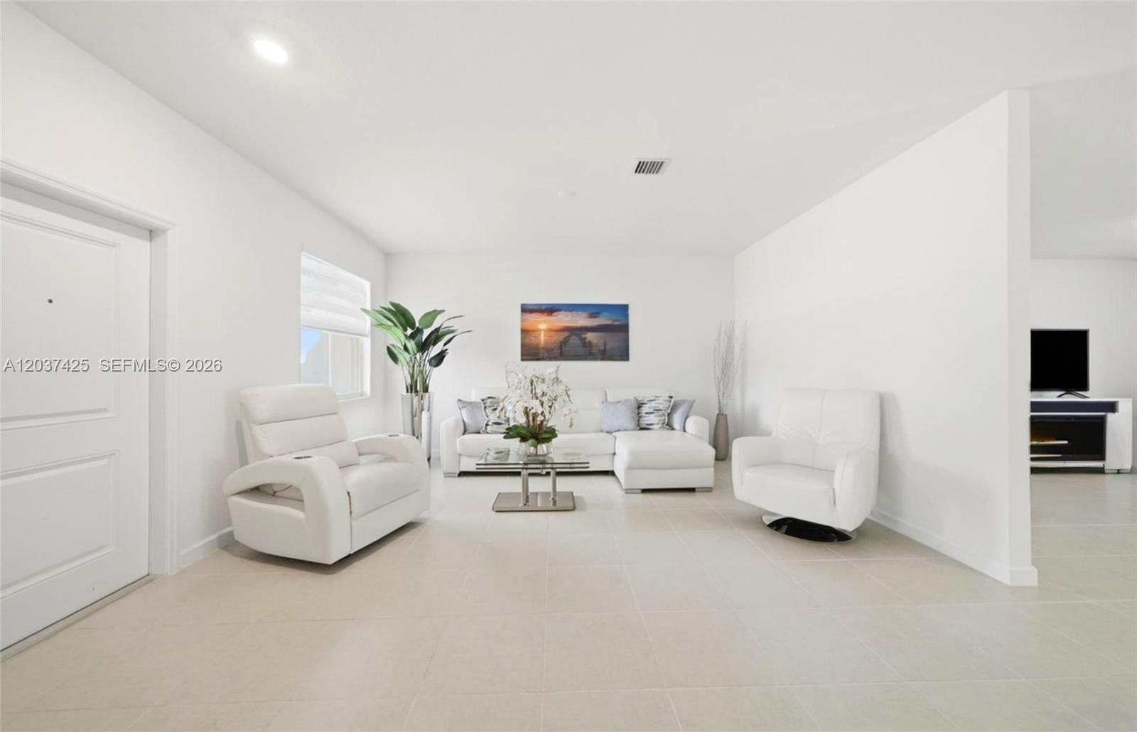 A bright living room features white furniture, tile flooring, and a sunset wall art piece — 13249 SW 189th Ter, Miami FL 33177, MIAMI, FL