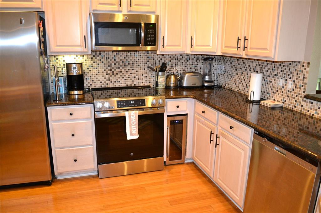 A kitchen features white cabinets, stainless steel appliances, a mosaic tile backsplash, and granite countertops — 11158 KAPOK GRAND CIRCLE, MADEIRA BEACH, FL