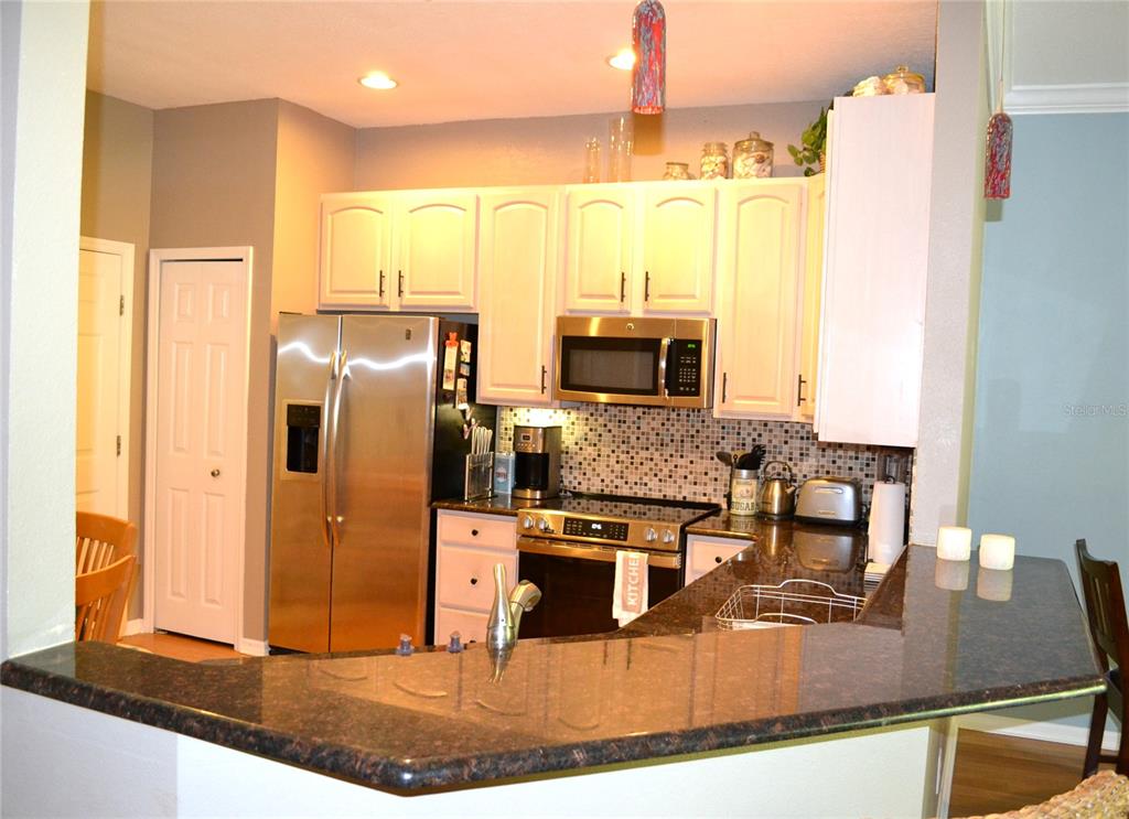 A kitchen features stainless steel appliances, white cabinets, and a dark granite breakfast bar — 11158 KAPOK GRAND CIRCLE, MADEIRA BEACH, FL