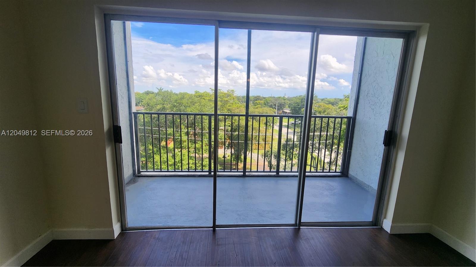 A room with dark wood flooring features a sliding glass door opening to a balcony — 7541 NW 16th St # 1507, Plantation FL 33313, PLANTATION, FL