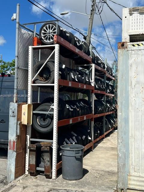 A tall metal storage rack holds numerous tires stacked outdoors next to a shipping container — NW 47th St, Miami FL 33142, MIAMI, FL