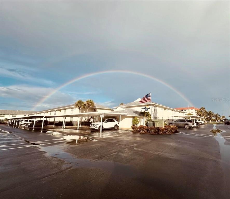 A rainbow arches over a multi-story apartment building with a parking lot and carports — 4225 S ATLANTIC AVENUE UNIT 236, NEW SMYRNA BEACH, FL