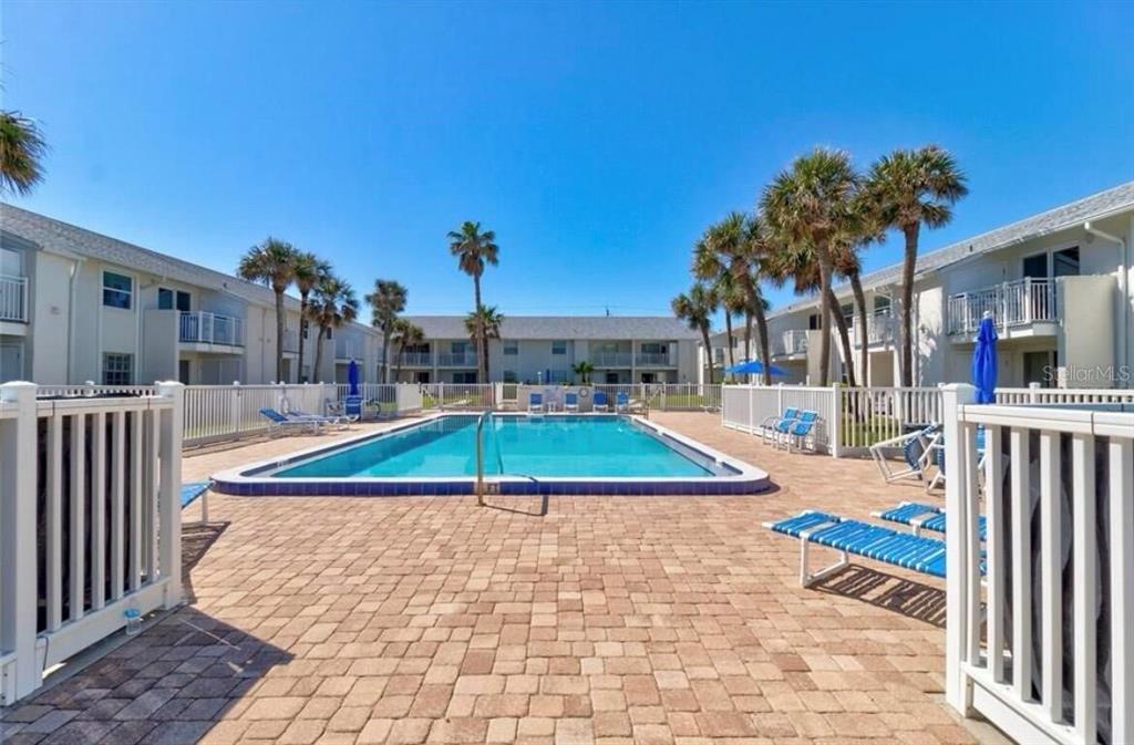 A rectangular swimming pool surrounded by a brick patio and palm trees between apartment buildings — 4225 S ATLANTIC AVENUE UNIT 236, NEW SMYRNA BEACH, FL