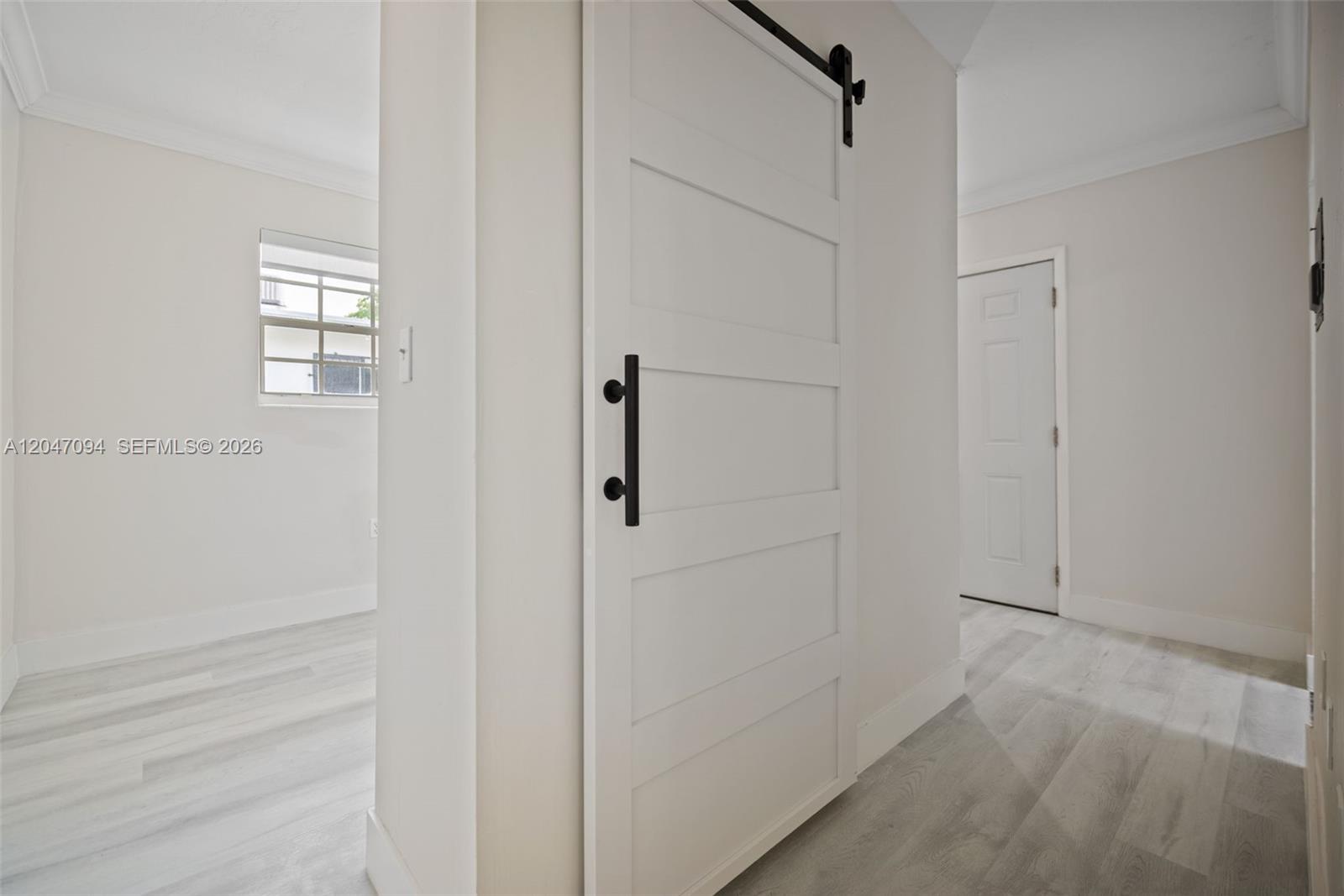A white barn door with black hardware stands in a hallway with light wood flooring — MIAMI, FL