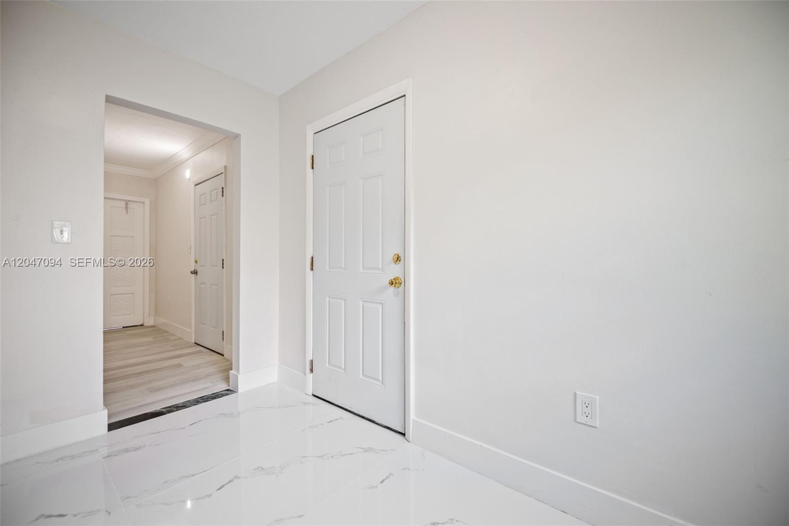 A white door stands in a room with white marble-look tile flooring and light walls — MIAMI, FL