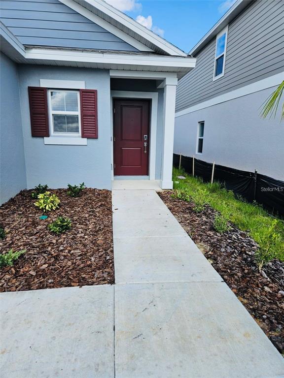 A blue house with a red front door and a concrete walkway leading to the entrance — 26220 FEATHERGRASS CIRCLE, LEESBURG, FL