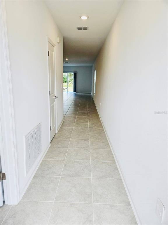 A long hallway with light-colored tile flooring leads toward a sliding glass door — 26220 FEATHERGRASS CIRCLE, LEESBURG, FL