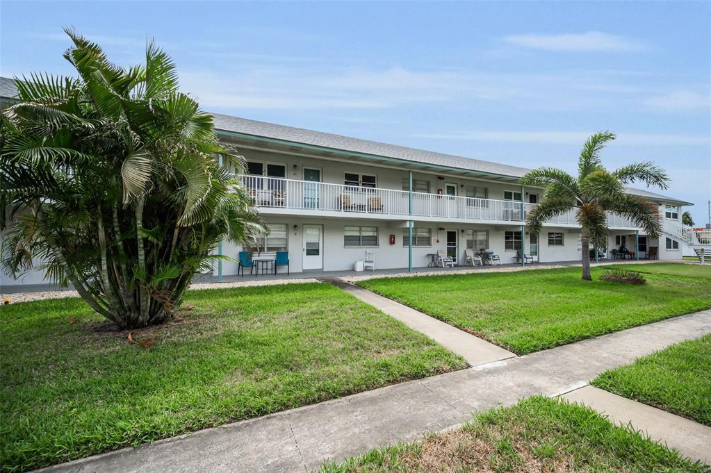 A two-story apartment building exterior features a white balcony, walkways, and palm trees at sunset — 5227 81ST LANE N UNIT 22, ST PETERSBURG, FL