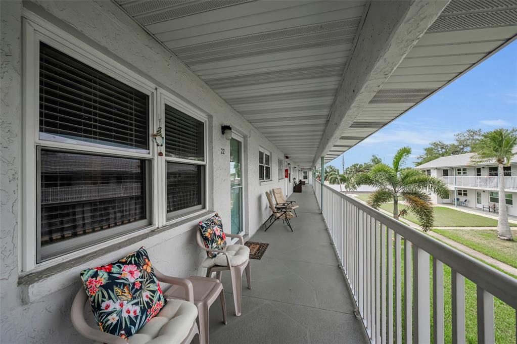An outdoor balcony walkway with chairs, railings, and a view of a neighboring apartment building — 5227 81ST LANE N UNIT 22, ST PETERSBURG, FL