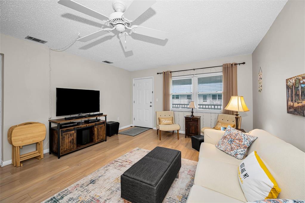 A living room features light wood flooring, a ceiling fan, a television console, and seating — 5227 81ST LANE N UNIT 22, ST PETERSBURG, FL
