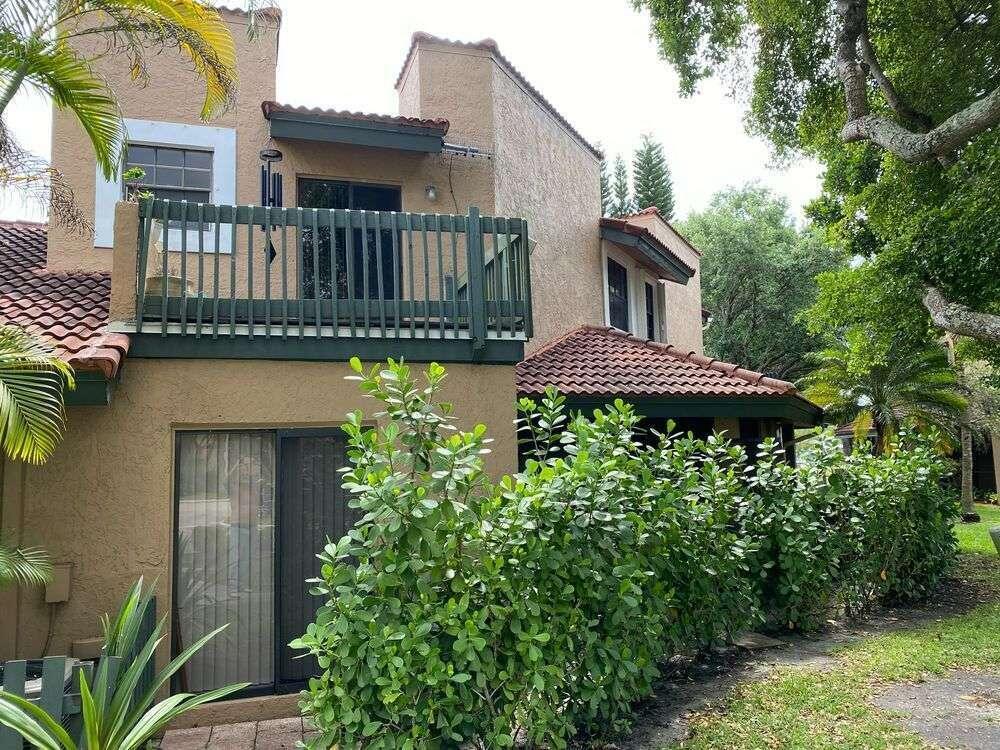 A two-story stucco house with a balcony, tile roof, and a hedge-lined patio — 9231 W Sunrise Boulevard, Plantation FL 33322, PLANTATION, FL