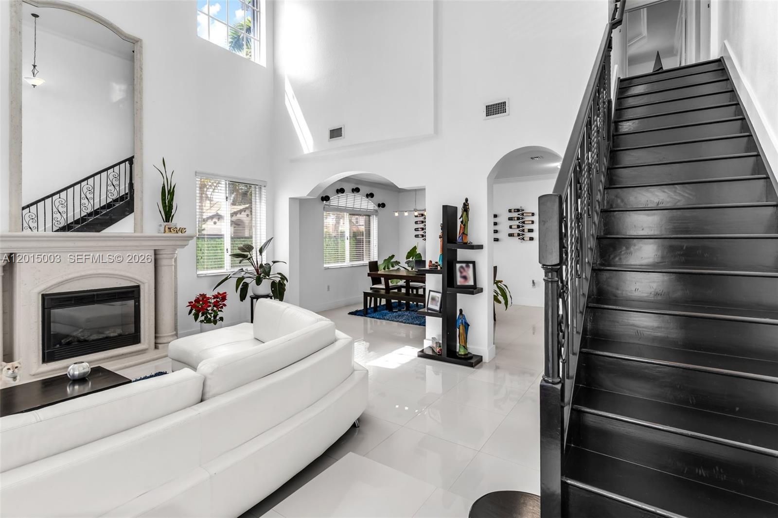 A bright living room features a fireplace, white sofa, and a dark wooden staircase — 15395 SW 23rd St, Miami FL 33185, MIAMI, FL
