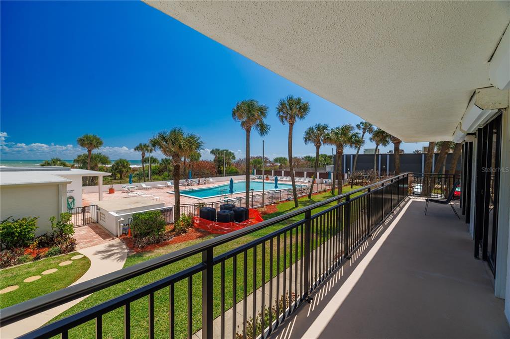 A balcony overlooks a swimming pool, palm trees, and the ocean in the distance — 2100 N ATLANTIC AVENUE UNIT 201, COCOA BEACH, FL