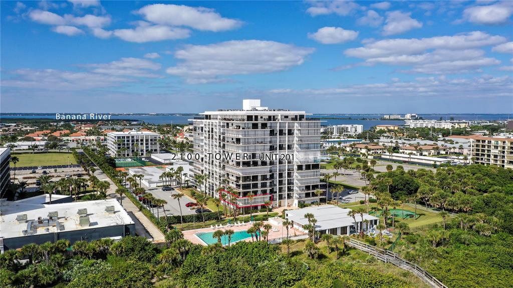 An aerial view shows a multi-story residential building with a pool and surrounding landscape — 2100 N ATLANTIC AVENUE UNIT 201, COCOA BEACH, FL