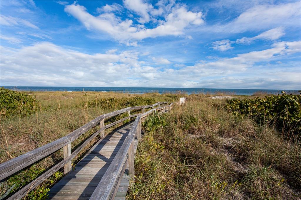 A wooden boardwalk leads through sand dunes toward the ocean under a cloudy sky — 2100 N ATLANTIC AVENUE UNIT 201, COCOA BEACH, FL