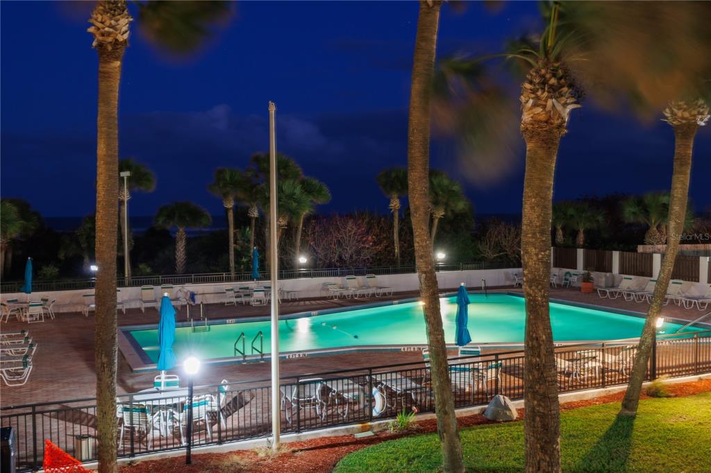 An outdoor swimming pool at night is surrounded by palm trees and a metal fence — 2100 N ATLANTIC AVENUE UNIT 201, COCOA BEACH, FL