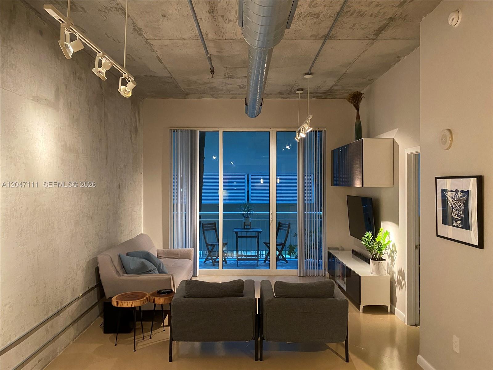 A living room features exposed concrete walls and ceilings, track lighting, and a balcony view — 2001 Biscayne Blvd # 3203, Miami FL 33137, MIAMI, FL