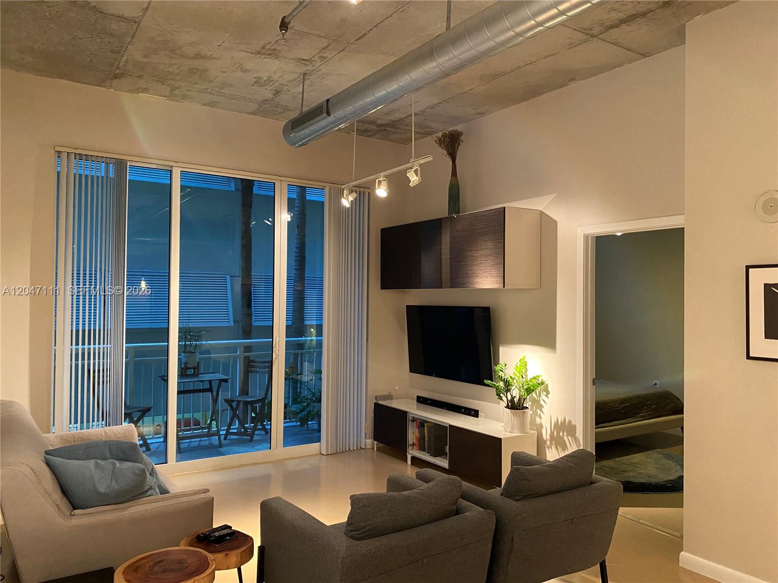 A living room features a concrete ceiling, exposed ductwork, a balcony, and modern furniture — 2001 Biscayne Blvd # 3203, Miami FL 33137, MIAMI, FL
