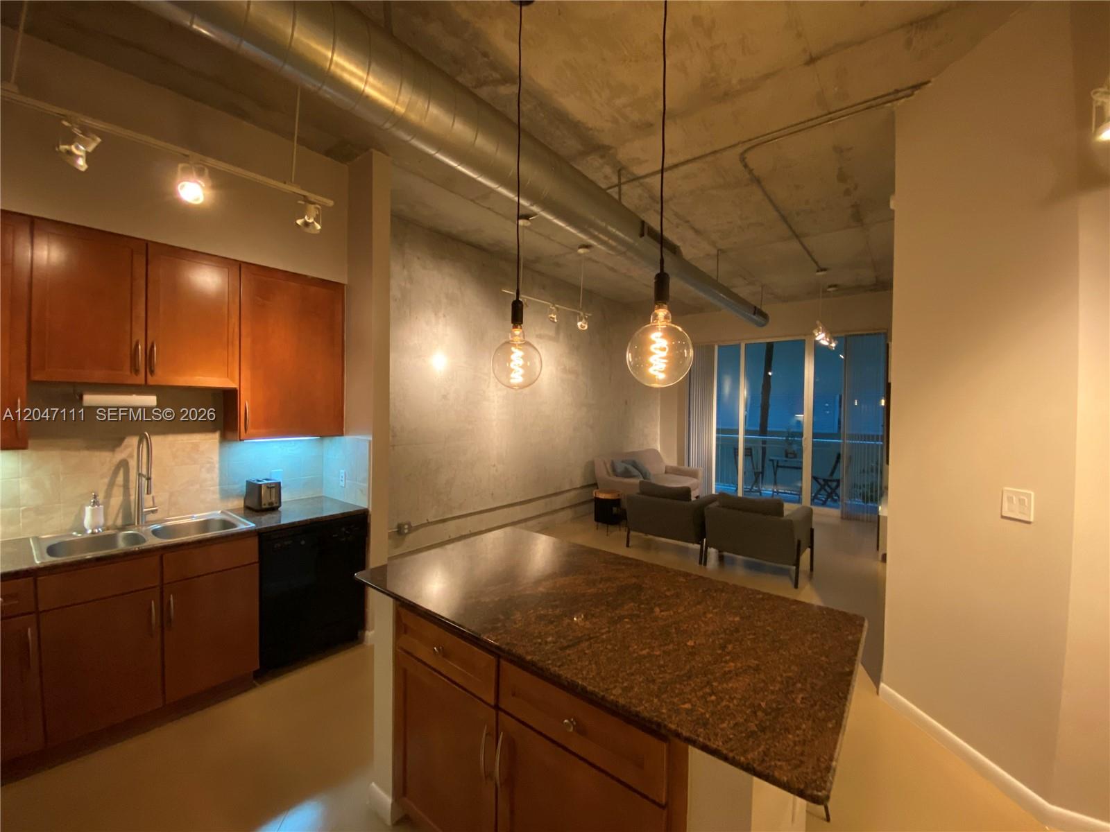 A kitchen with wood cabinets and a granite island opens into a living area — 2001 Biscayne Blvd # 3203, Miami FL 33137, MIAMI, FL