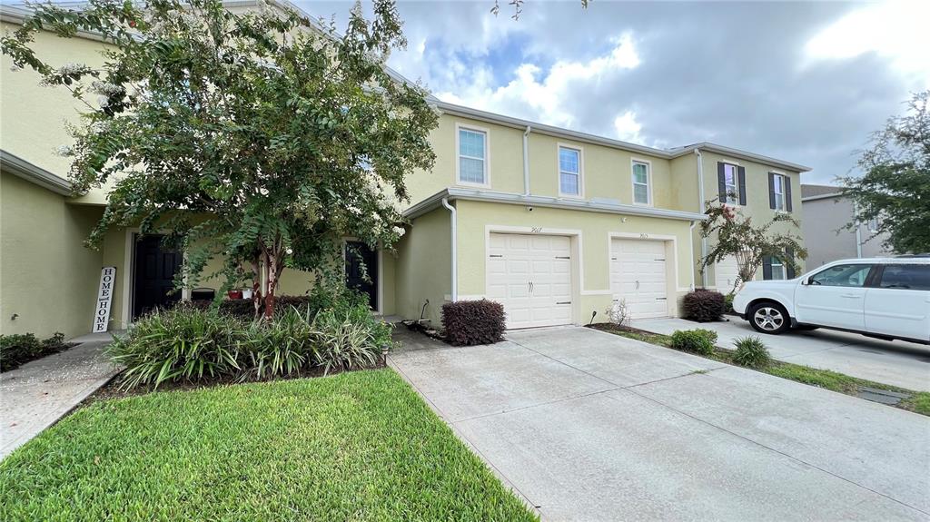 A two-story townhouse with a concrete driveway, a single-car garage, and a front yard tree — 9017 ALBA LANE, KISSIMMEE, FL